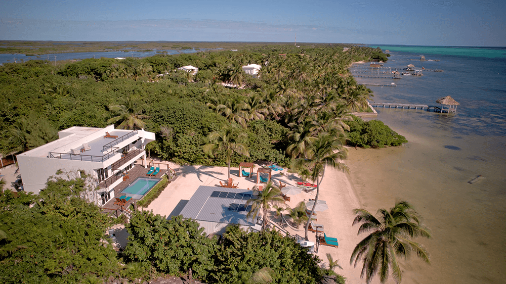 Aerial view of a coastal property with palm trees, a swimming pool, and piers extending into the water.